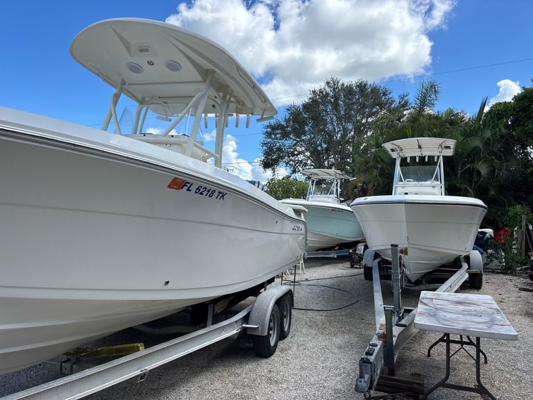 Two white recreational fishing boats parked on trailers outdoors with trees and blue sky in background