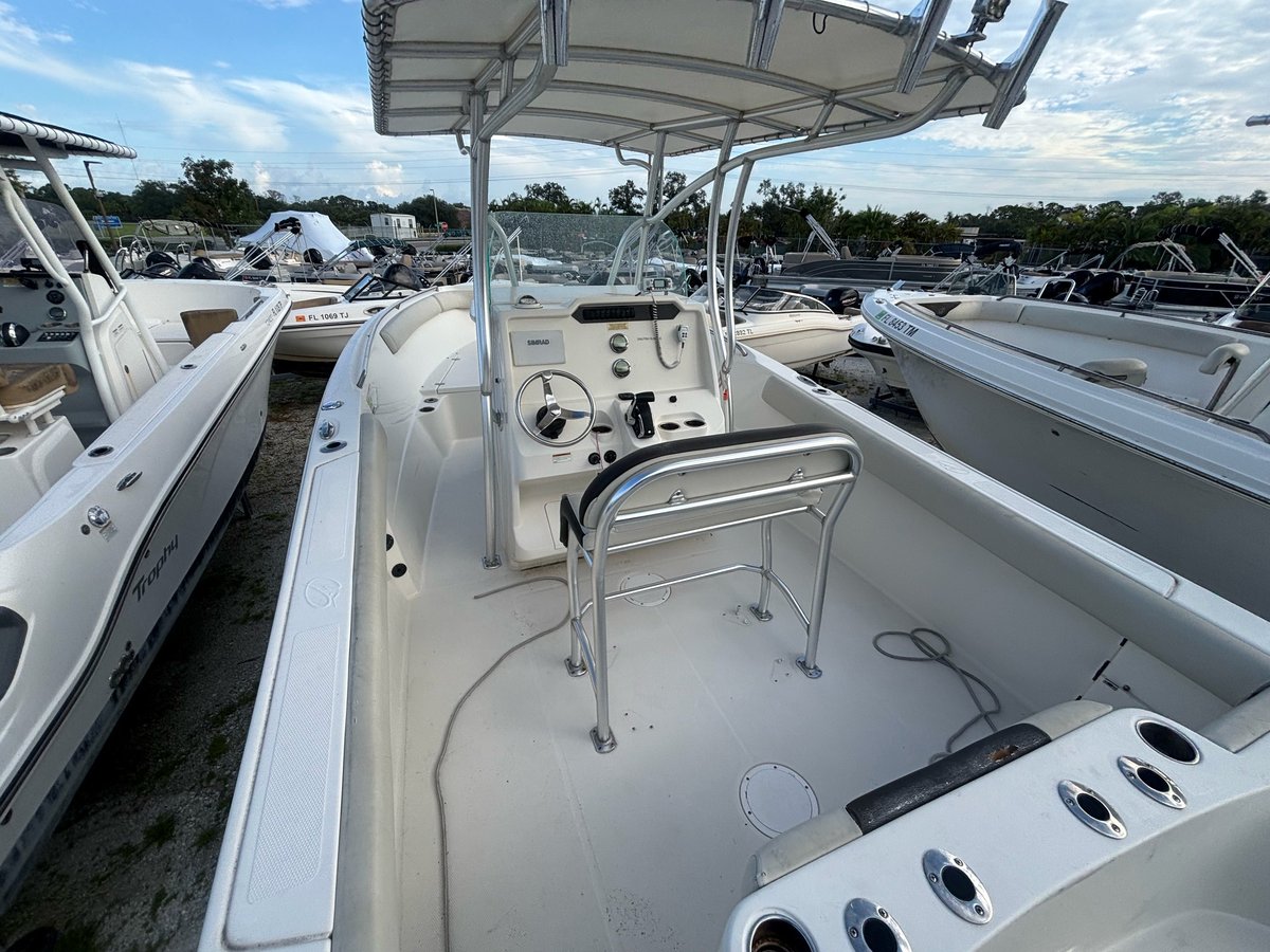 White fishing boat with open center console, hardtop canopy, and multiple deck features at a marina