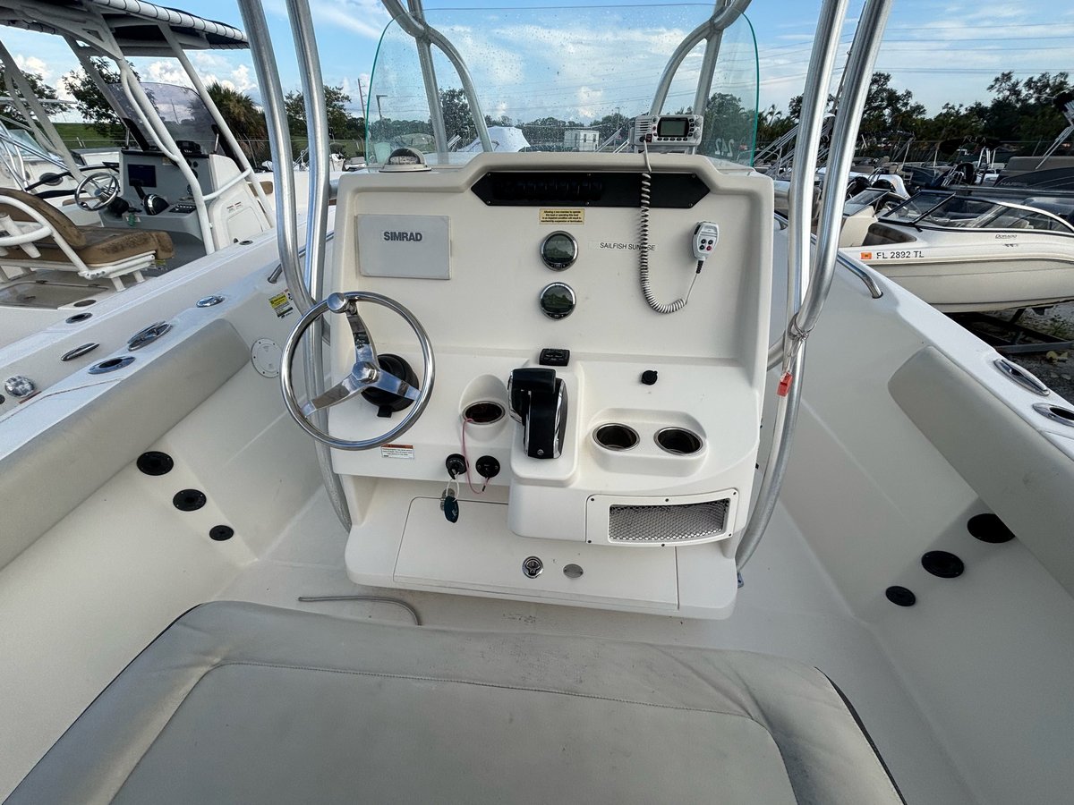 Interior view of a white center console fishing boat helm with steering wheel, control panel, and dashboard at a marina